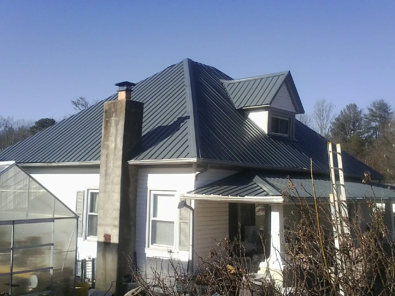 Dark blue standing seam metal roof on a white farmhouse with dormer — Slate & Tile Roof Repair by Roofing Brothers in High Springs