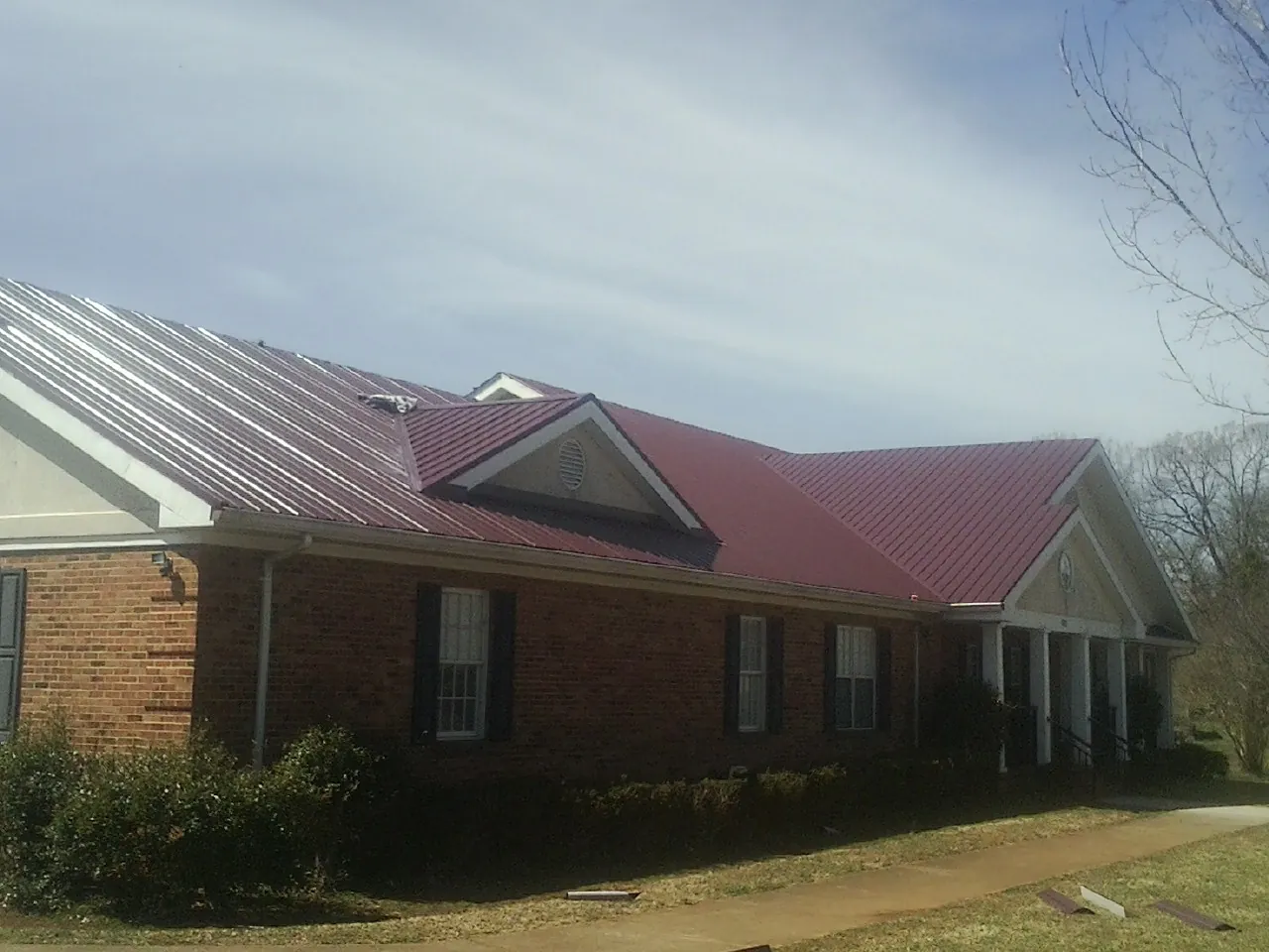 Red metal roof with gabled entries on a long brick building, from a Hail Damage Roof Repair job in High Springs