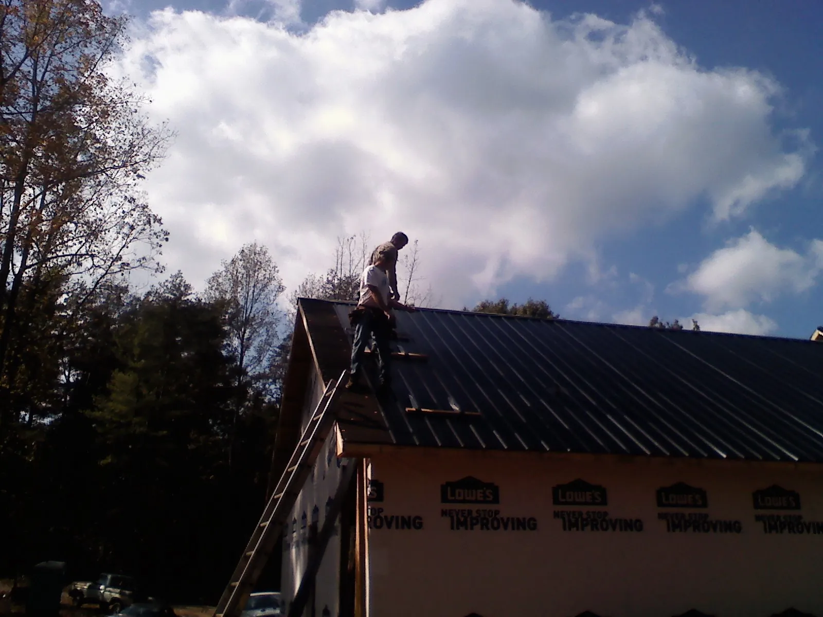 Roofer fastening dark metal panels high against a cloudy sky, from a Roof Inspection job in High Springs