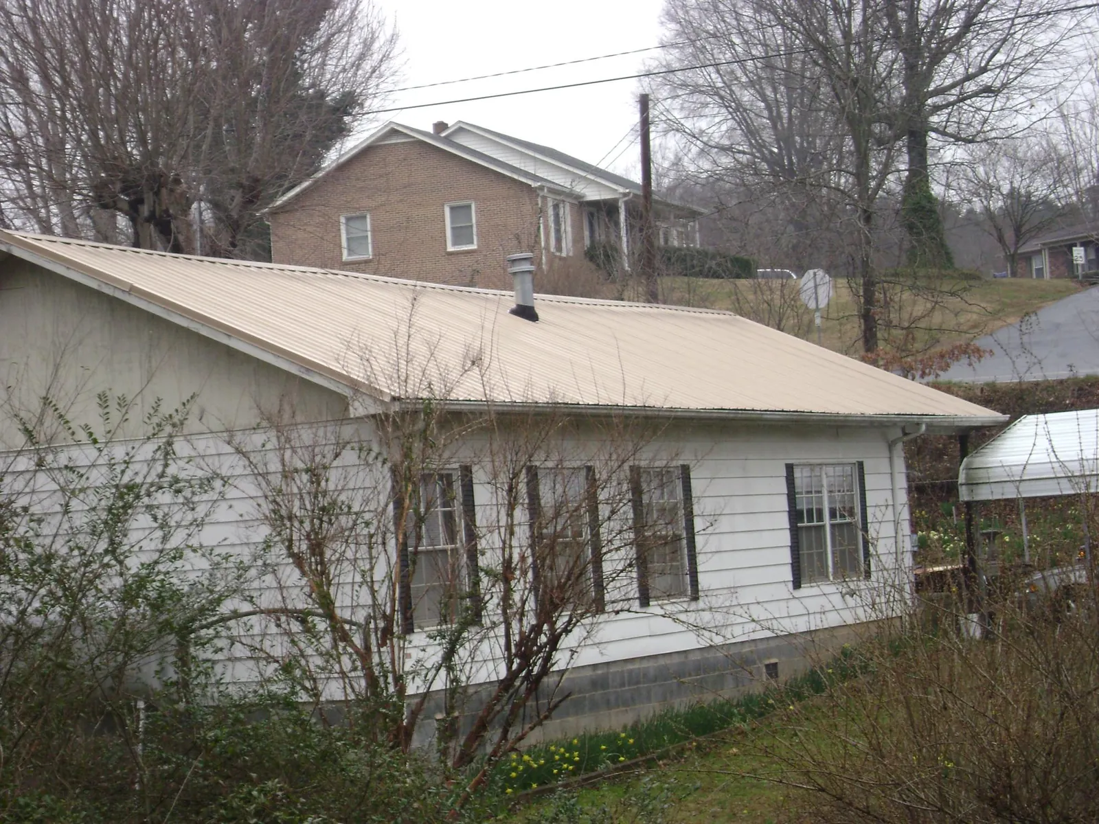 Tan metal roof on a white sided house set into a hillside — Commercial Roofing by Roofing Brothers in High Springs